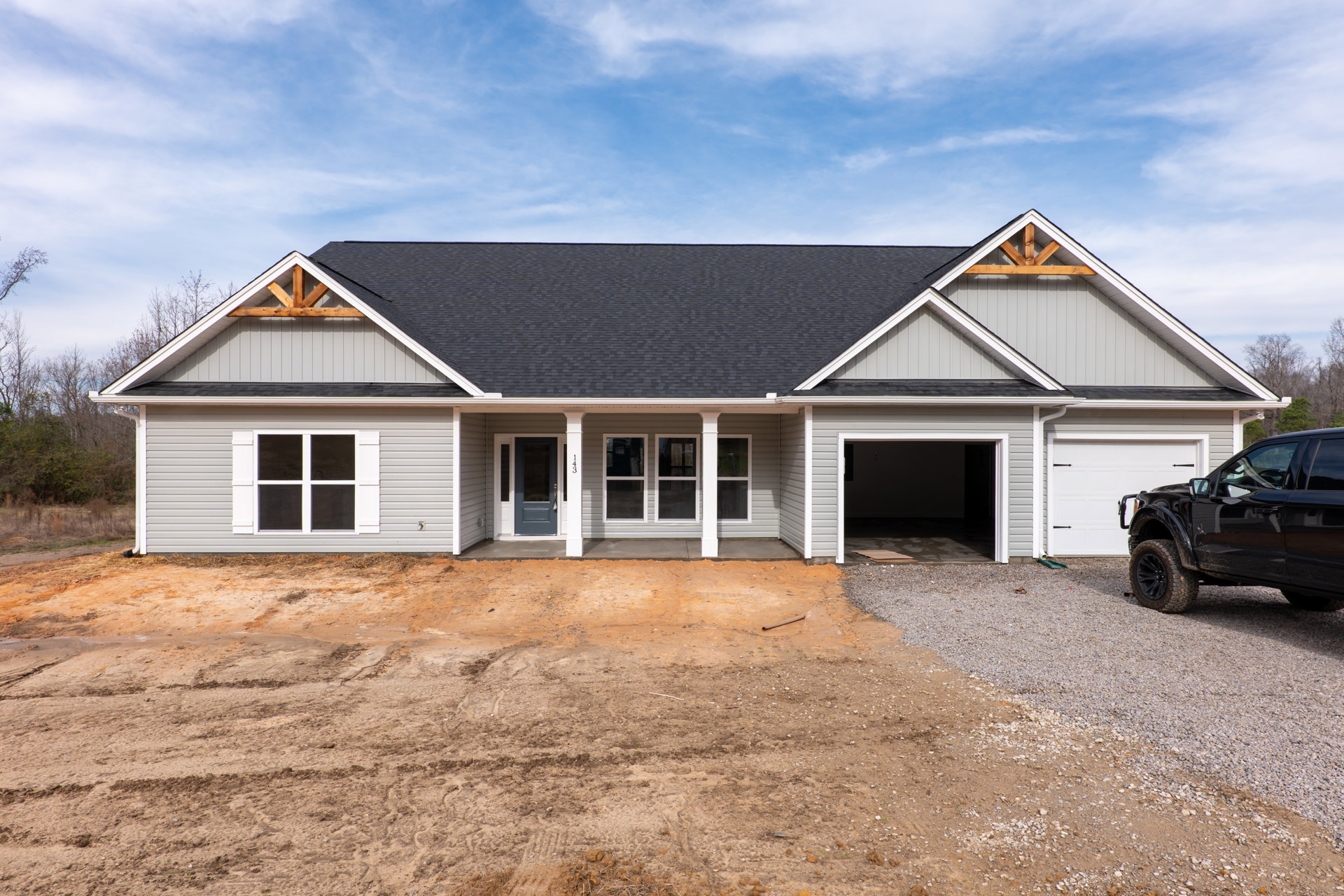 Two-story house with white pillars, grey front door, open garage, black truck parked in driveway, white-framed windows, cloudy sky overhead
