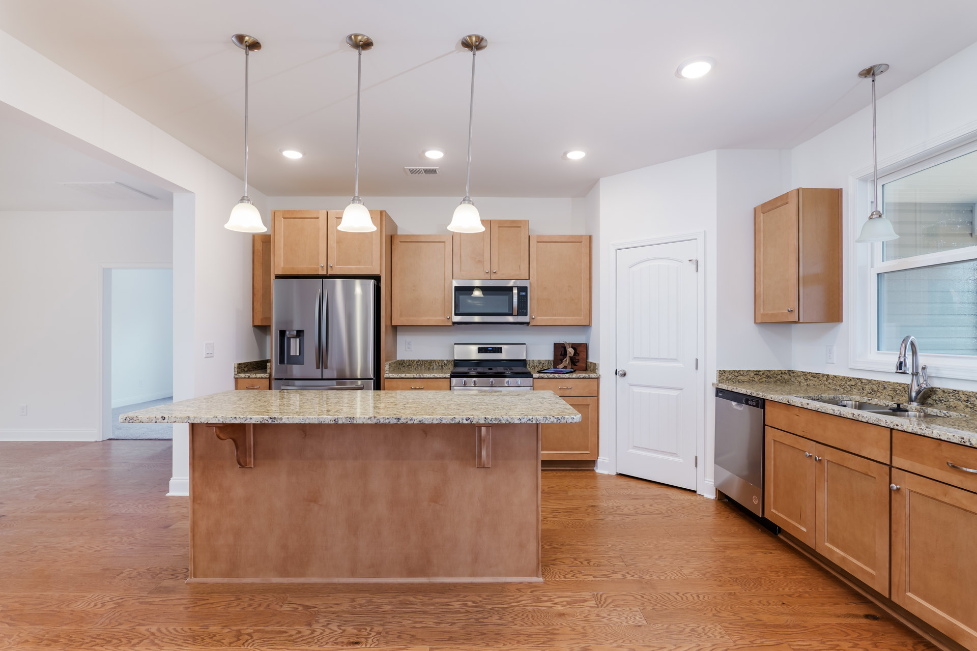 Spacious kitchen featuring a large central island with white quartz countertop, stainless steel refrigerator with water dispenser, built-in microwave, white cabinetry, and light