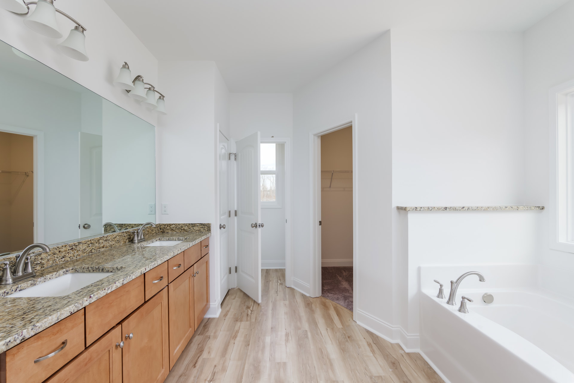 Bathroom with polished marble floor, freestanding white bathtub, double sinks set in wooden cabinets, chrome faucets, and a close-up of a lamp shade.