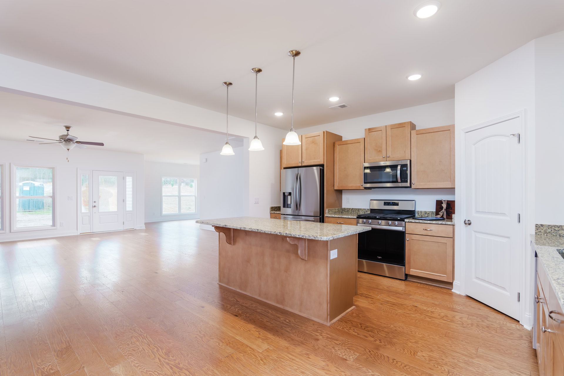 Kitchen with wood flooring, central island featuring granite countertop, stainless steel double-door refrigerator, built-in microwave with underlighting, stove, white cabinetry