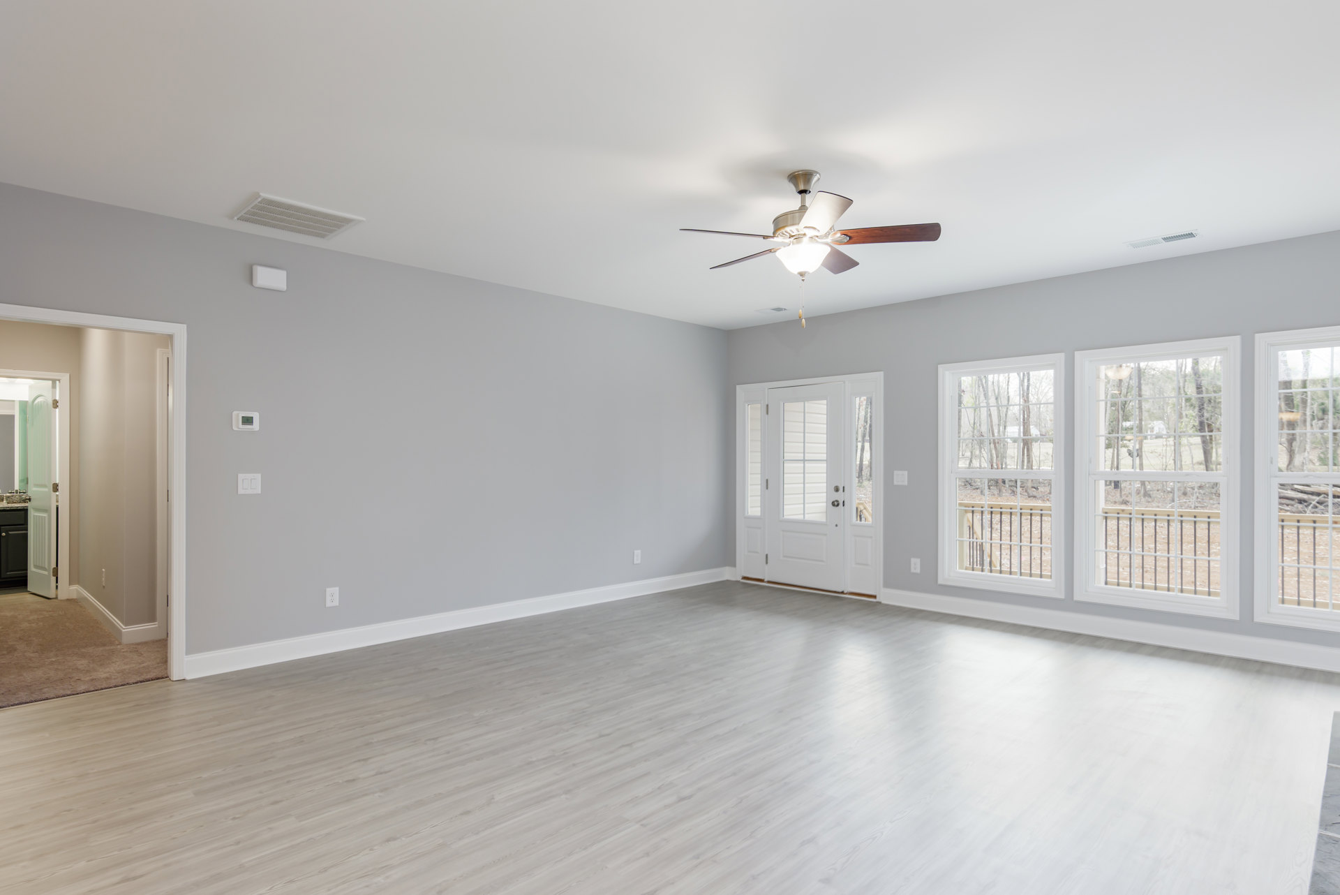 White room with wood flooring, ceiling fan with light, white door featuring glass panes, row of windows showing trees outside