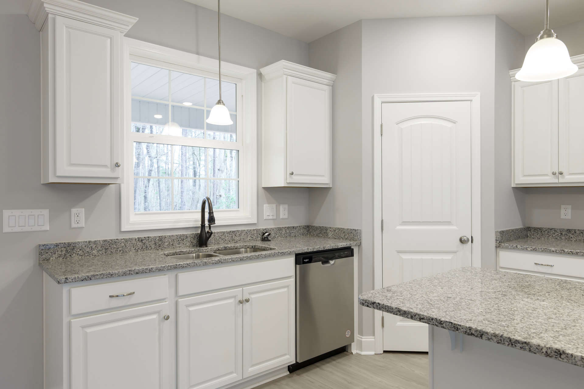 Granite countertops, stainless steel sink, white cabinetry, white refrigerator with red and white sticker, ceiling light fixture, white surface on adjacent counter
