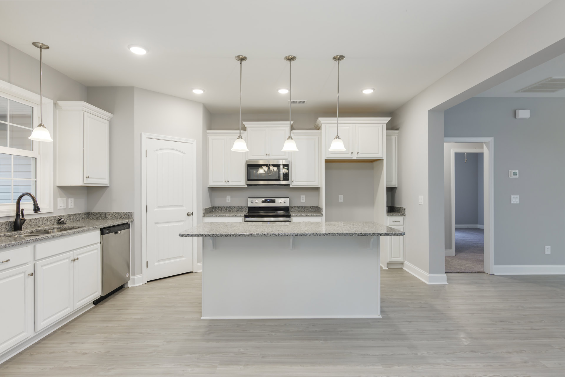 Open kitchen with white shaker cabinets, marble countertop bar, stainless steel oven, built-in microwave, pendant light fixture, and light wood flooring