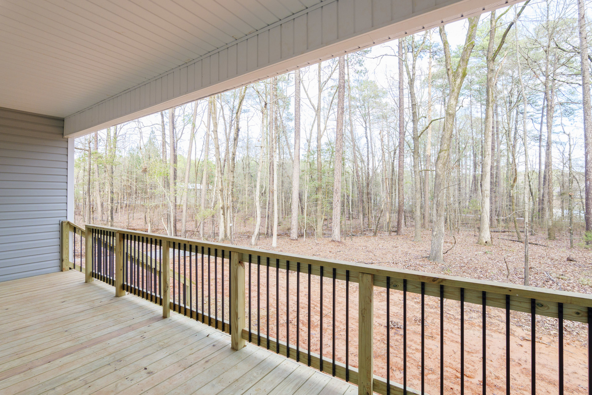Wooden deck with metal railing overlooking dense forest, trees visible beyond fence, close-up of wooden post in foreground