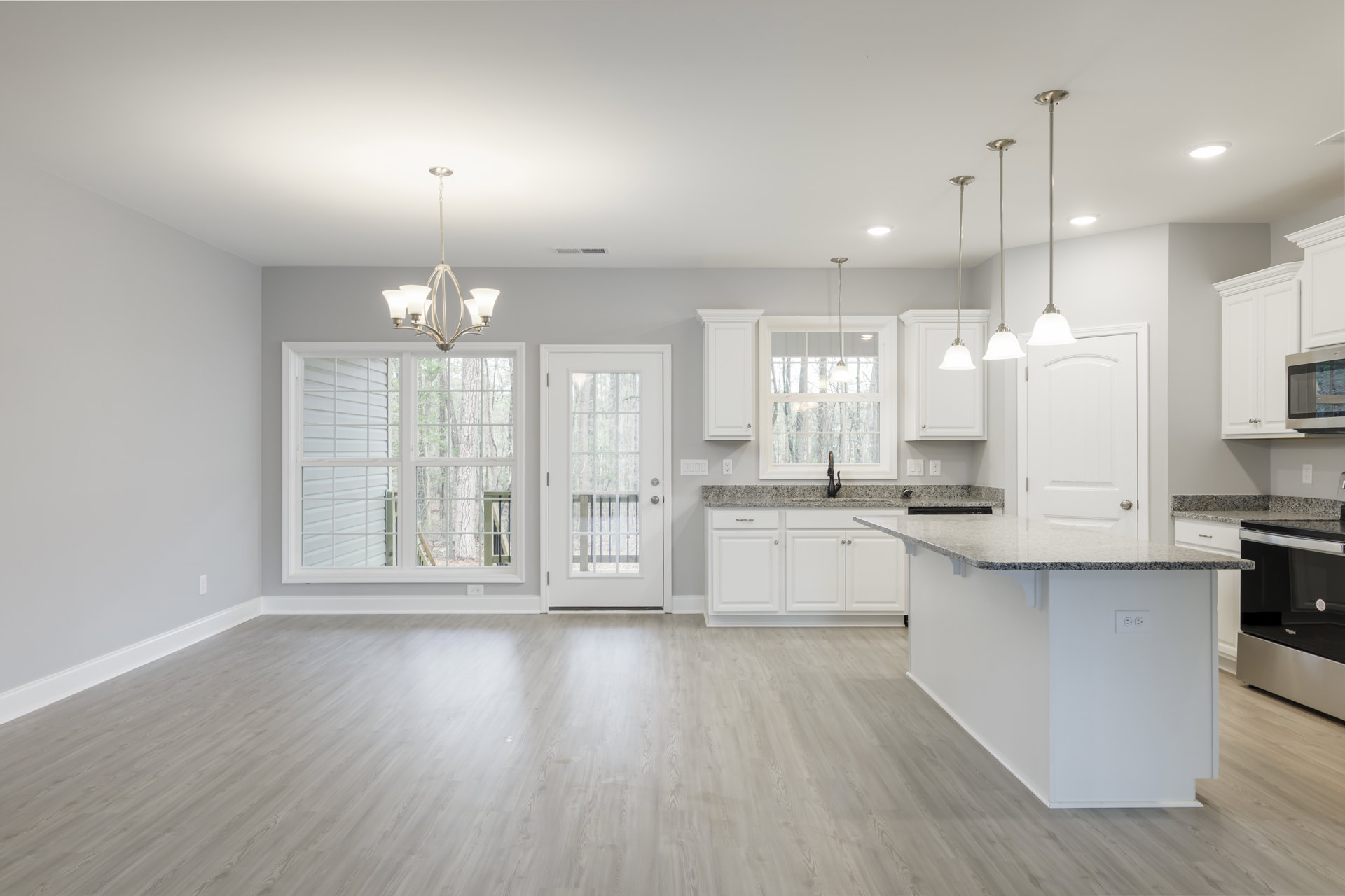 Open kitchen and dining area featuring white cabinetry, granite countertops, wood flooring, black and silver refrigerator, glass-paneled white door, and a metal support pole.