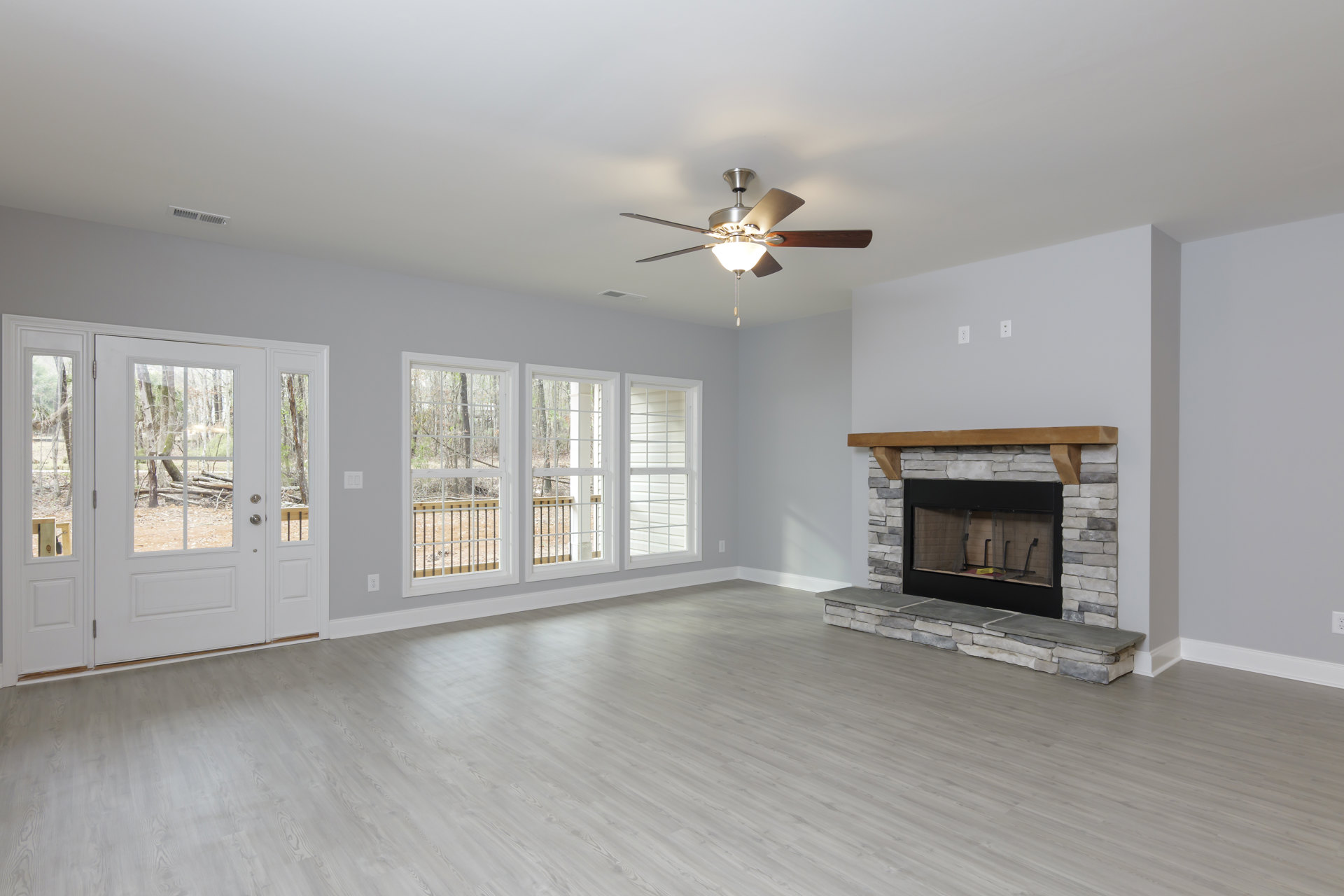 Living room with wood flooring, central fireplace featuring a black door and wood mantel, ceiling fan with light fixture, window with white trim, and a small table.