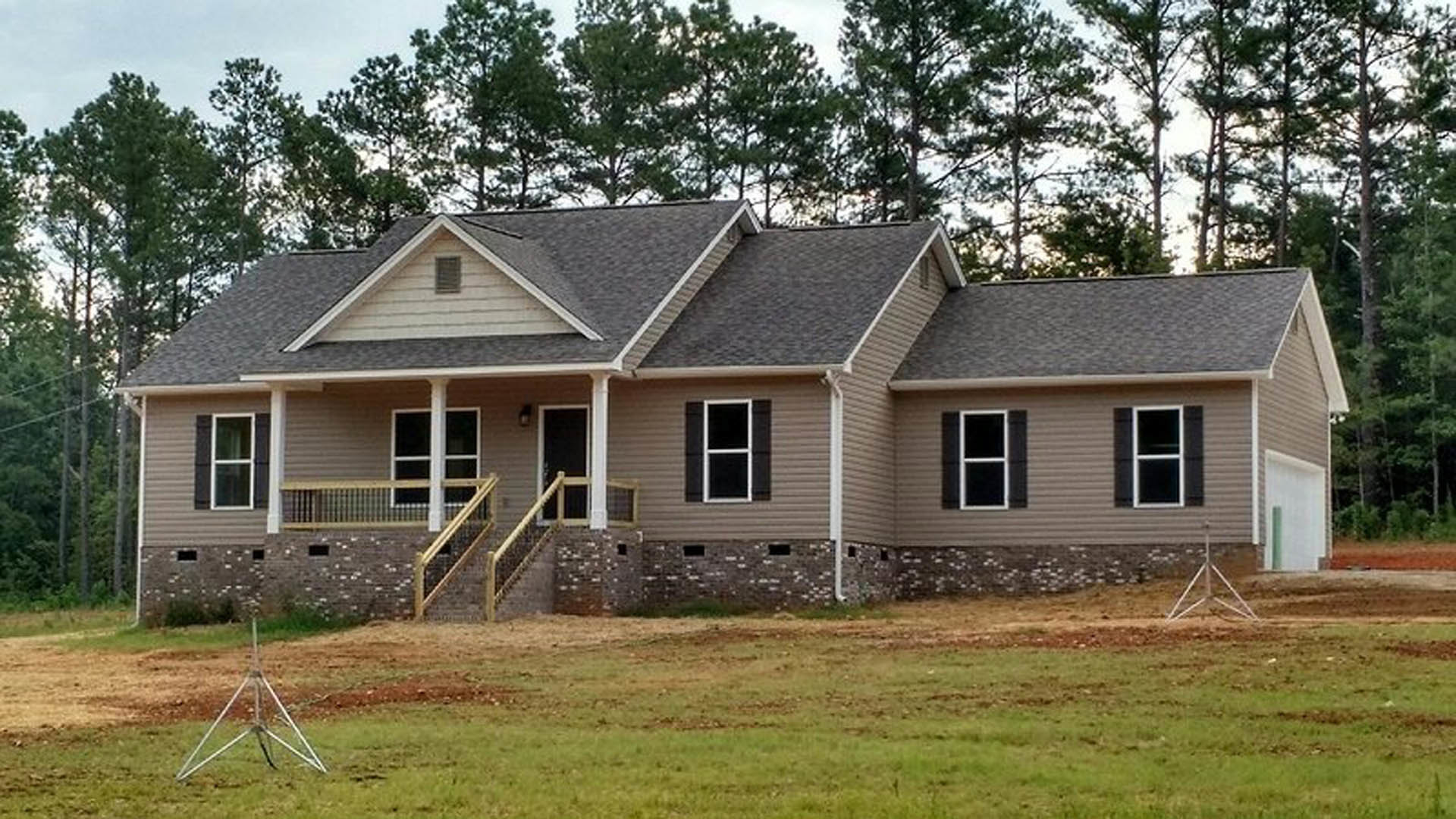 Two-story white house with covered porch, white-framed windows, front stairs, manicured lawn, mature trees, and blue sky in background
