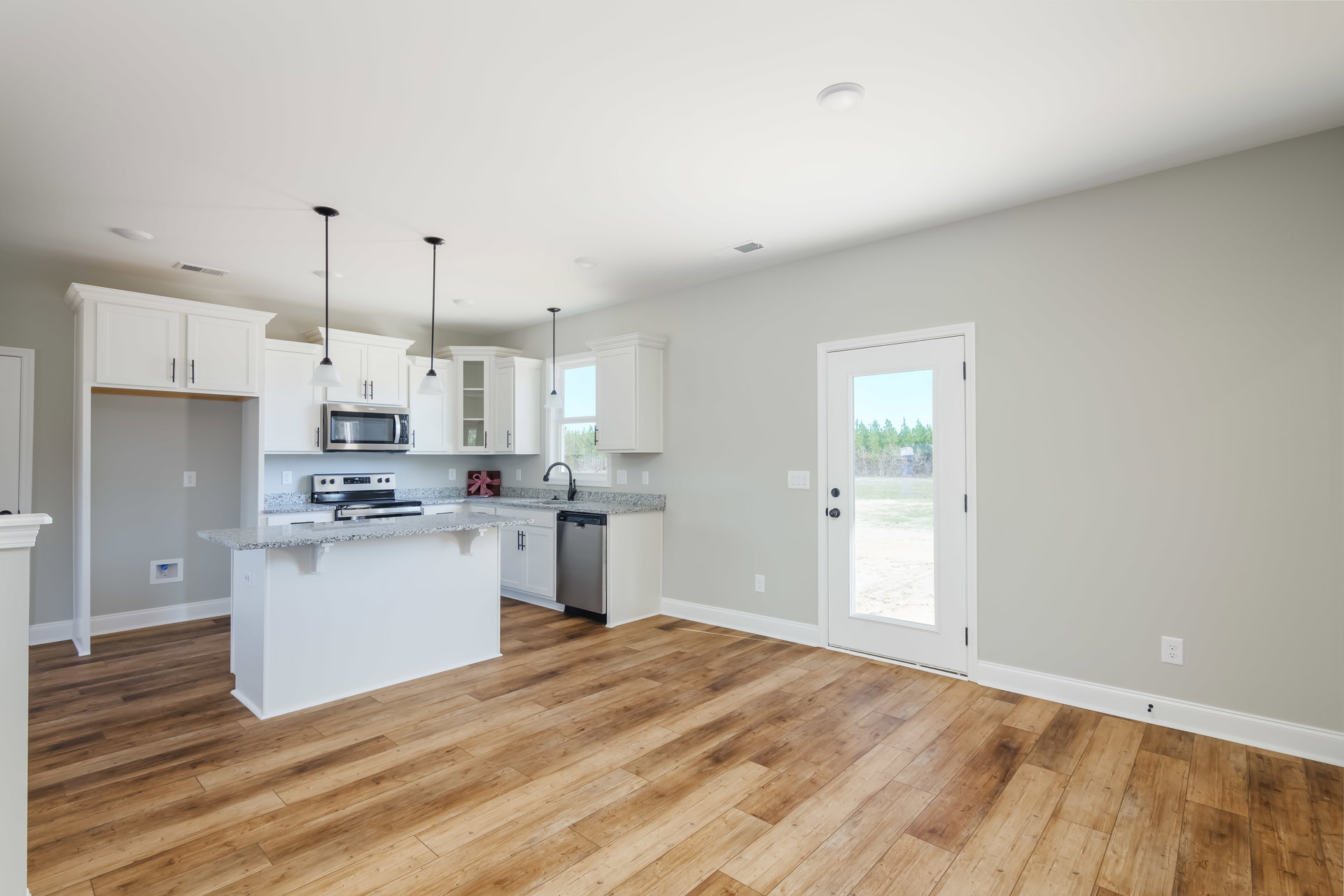 Open kitchen and dining area featuring wood flooring, white walls, glass-paneled door, built-in microwave, cabinetry, and large window.
