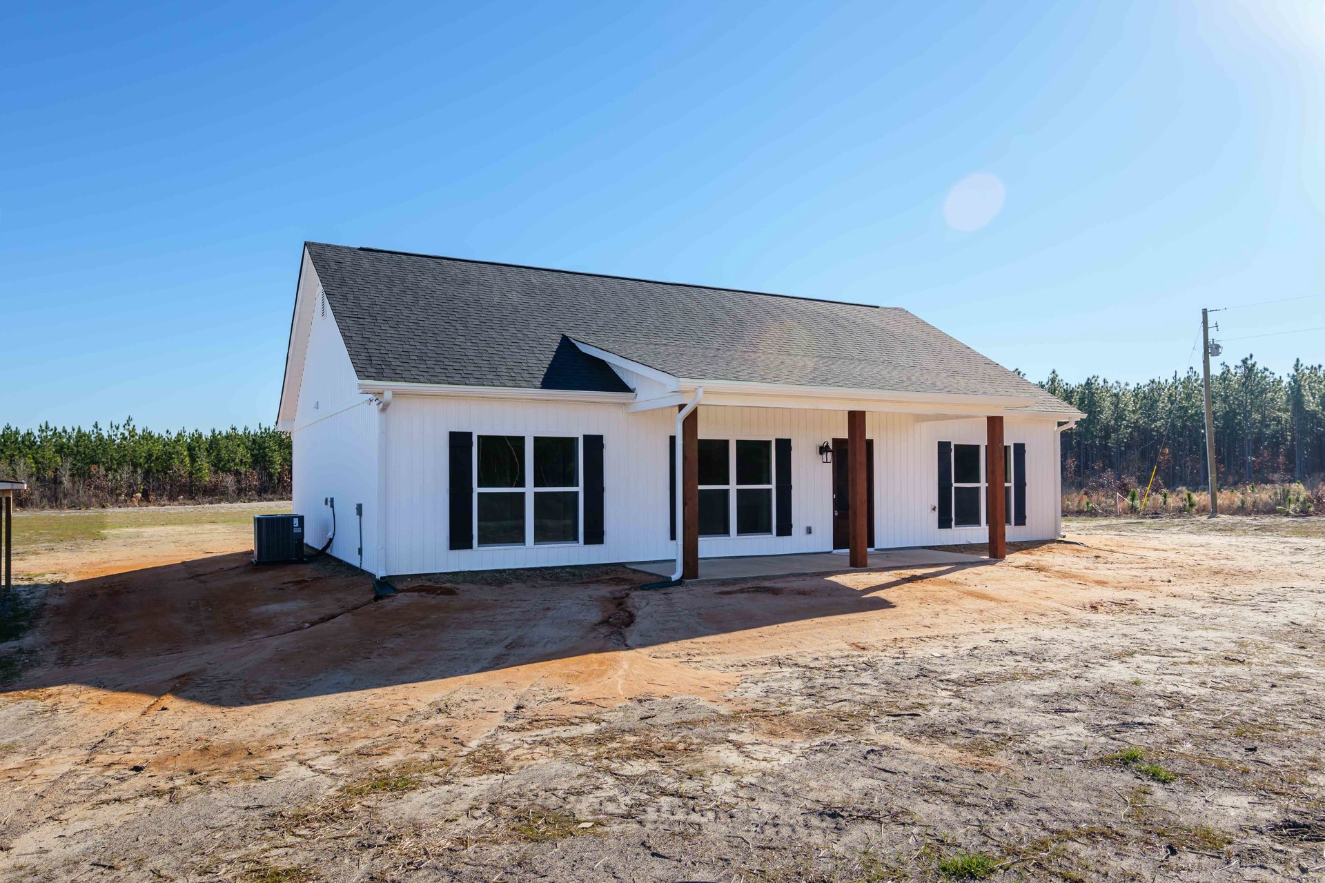 White house with black roof, dirt area in front, dirt road beside, close-up window, black rectangular object with white label near exterior.