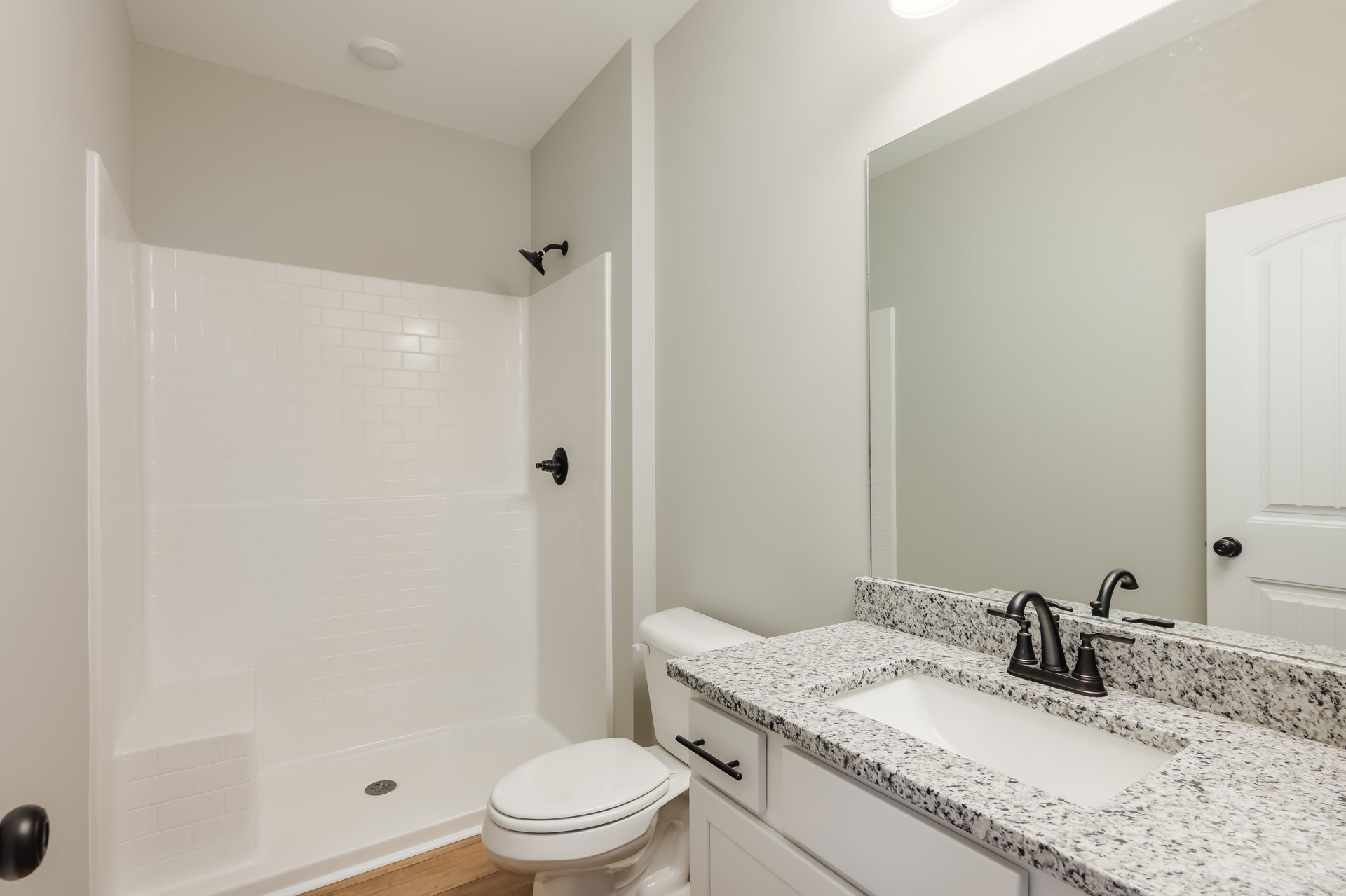 Modern bathroom with white tile walls, black wall-mounted lamp, black faucet on a white countertop, sink, and closed white toilet.
