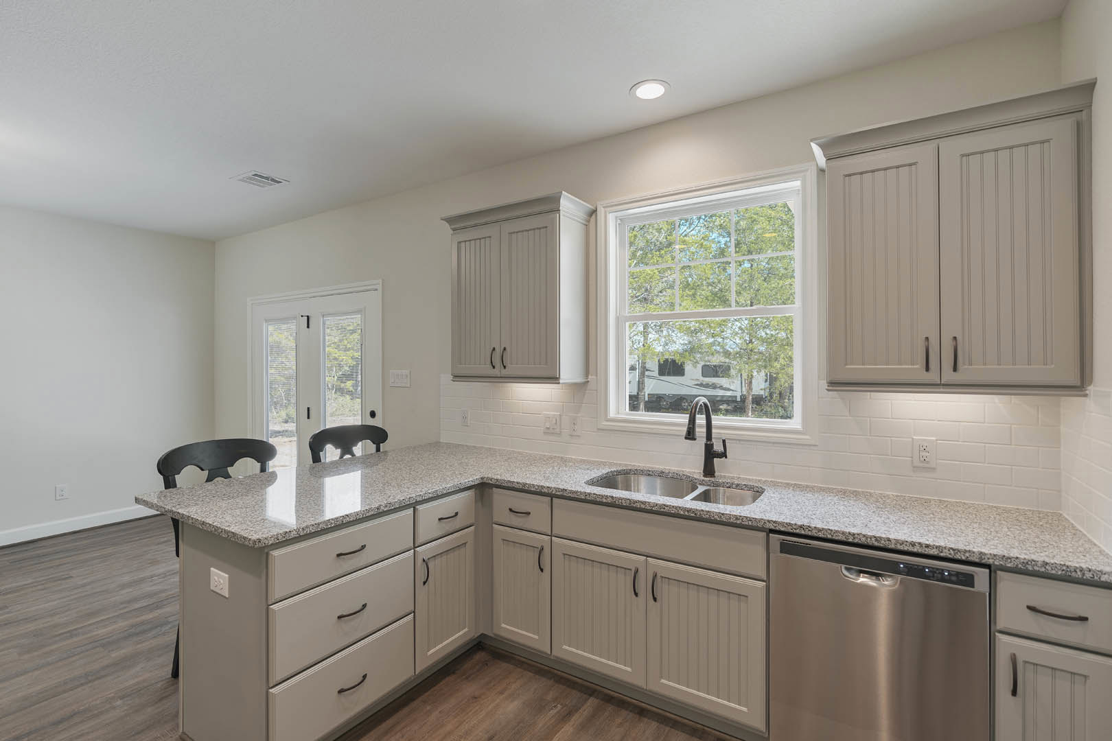 White shaker cabinets with black handles, stainless steel dishwasher, undermount sink set in light quartz countertop, large window overlooking trees and camper