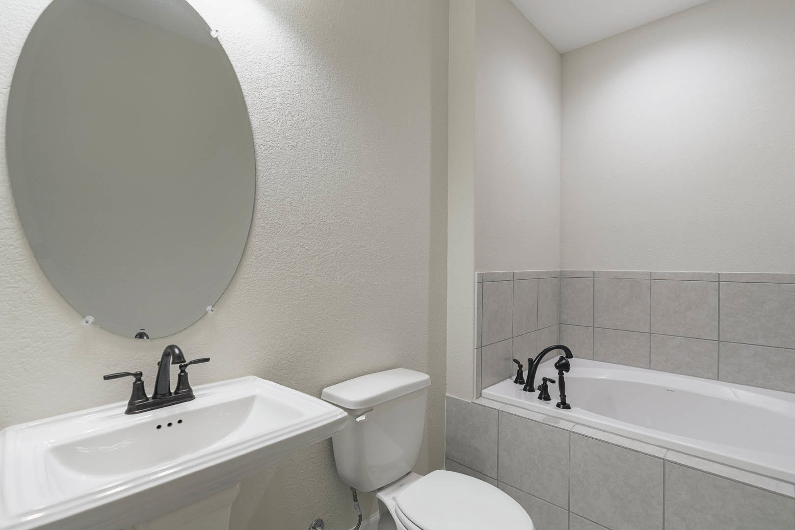 Modern bathroom featuring a freestanding bathtub with chrome faucet, white ceramic sink set in a stone countertop, tiled walls, and a wall-mounted toilet.