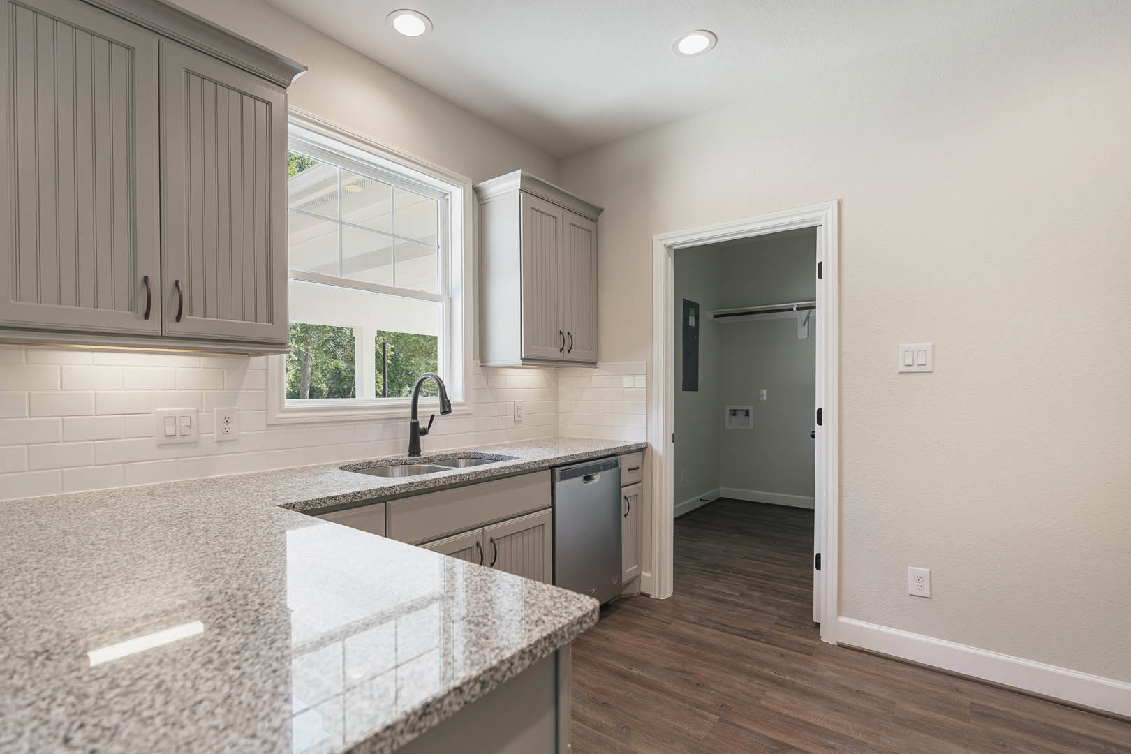Granite countertops, wood flooring, multi-pane window, white cabinetry, stainless steel sink, white double light switch on wall