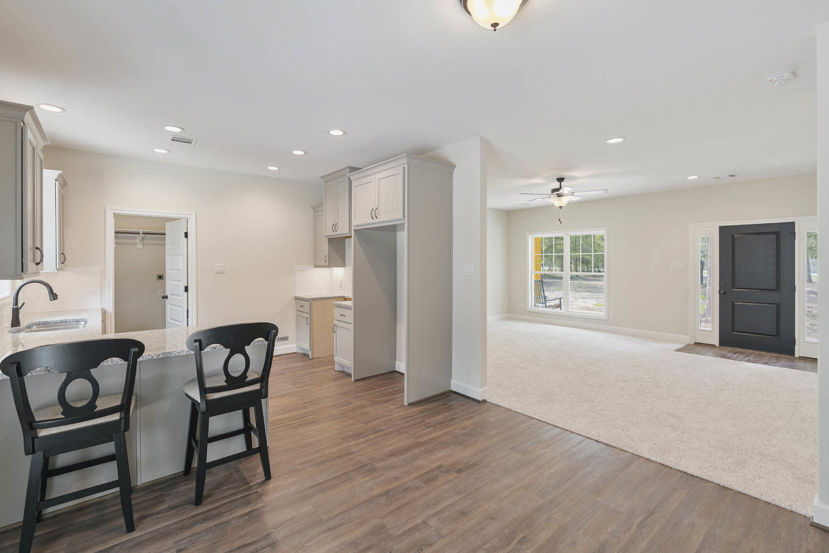 Open kitchen and living room featuring wood flooring, marble-topped counter with cushioned chairs, white cabinetry, recessed lighting, and large windows with outdoor seating