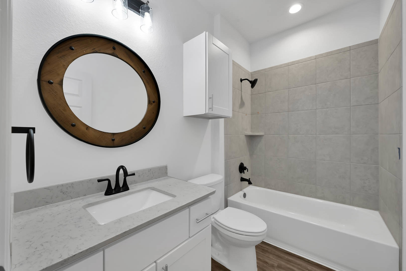 Bathroom with white tile walls, white cabinet under sink, black curved faucet, wall-mounted mirror, freestanding white bathtub beside toilet, ceiling light fixture