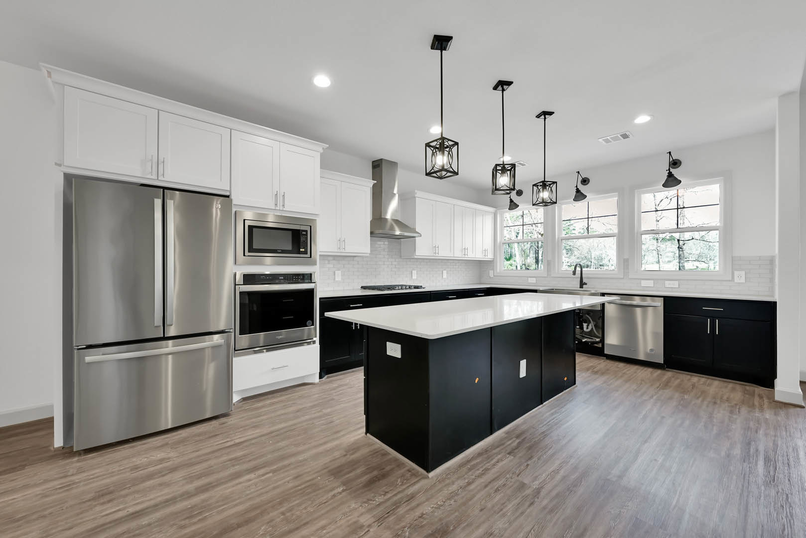 Spacious kitchen featuring a large central island with black and white finishes, stainless steel refrigerator and microwave, white cabinetry, and light countertops