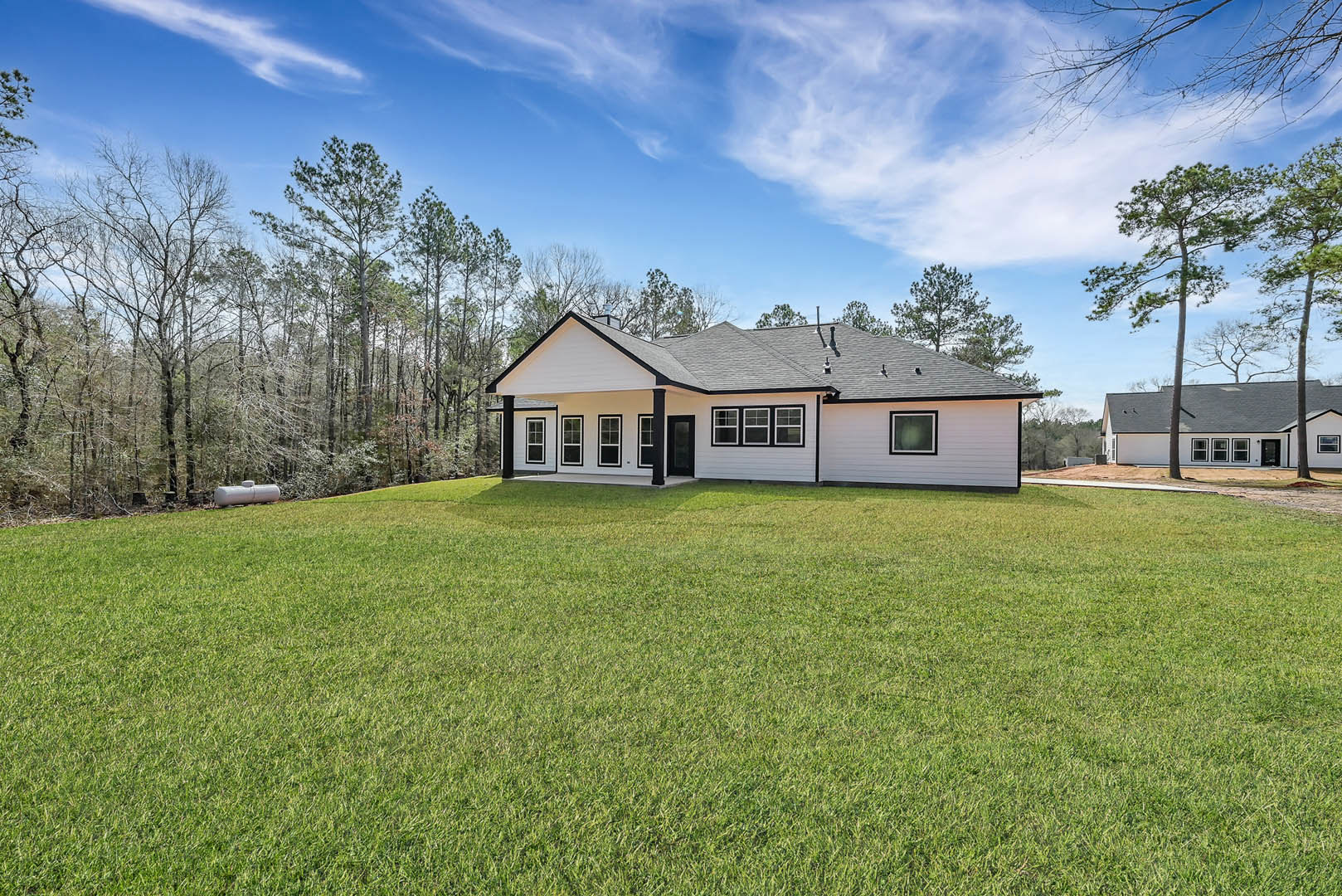 White farmhouse with black trim and columns, black roof, manicured green lawn, mature trees in background, partly cloudy sky