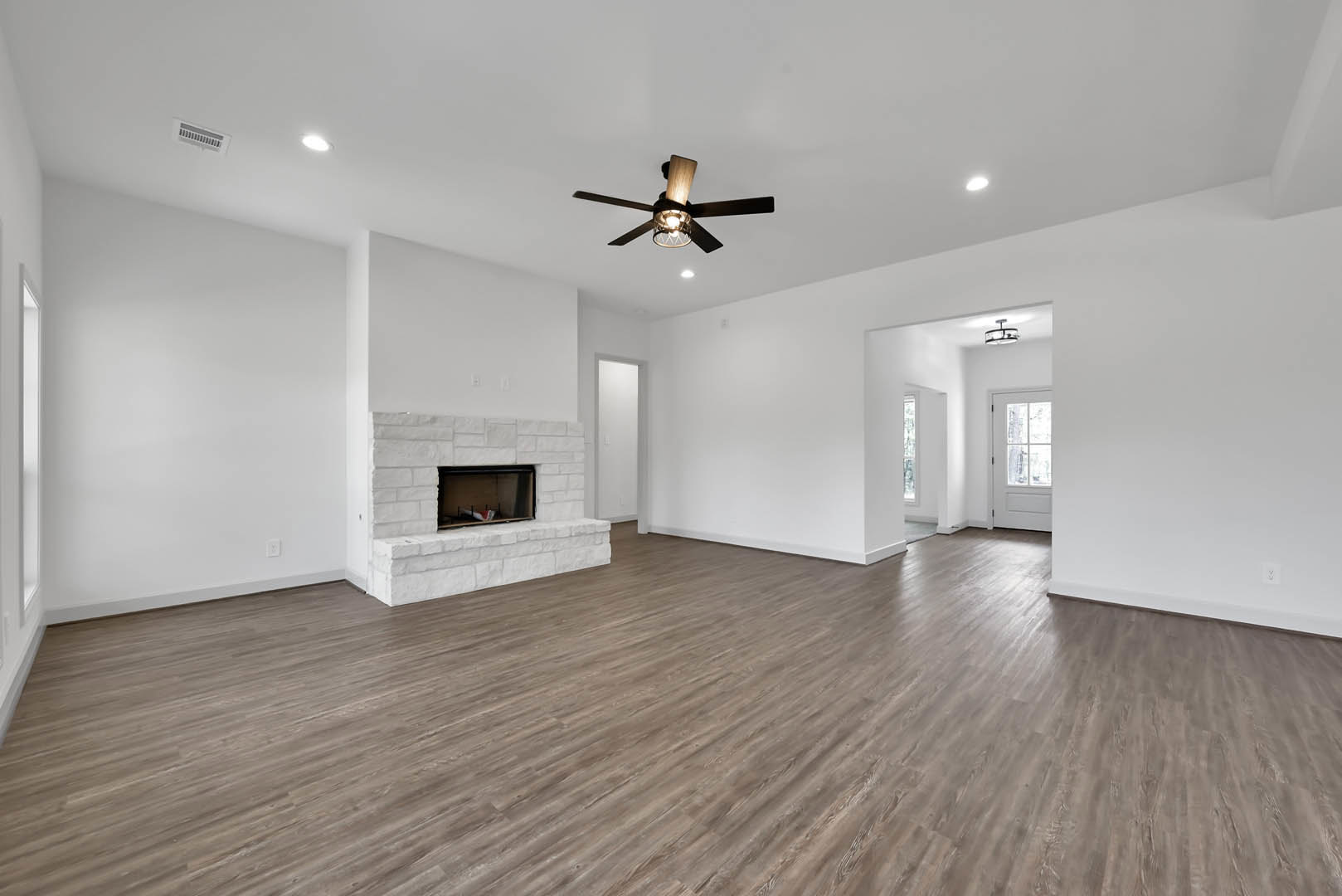 Living room with brick fireplace, wood laminate flooring, ceiling fan with light, white door featuring window, and plaster walls.