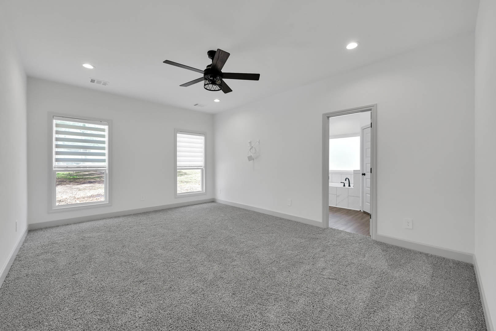 Carpeted room with white blinds on a large window, ceiling fan with light fixture, neutral walls and white trim