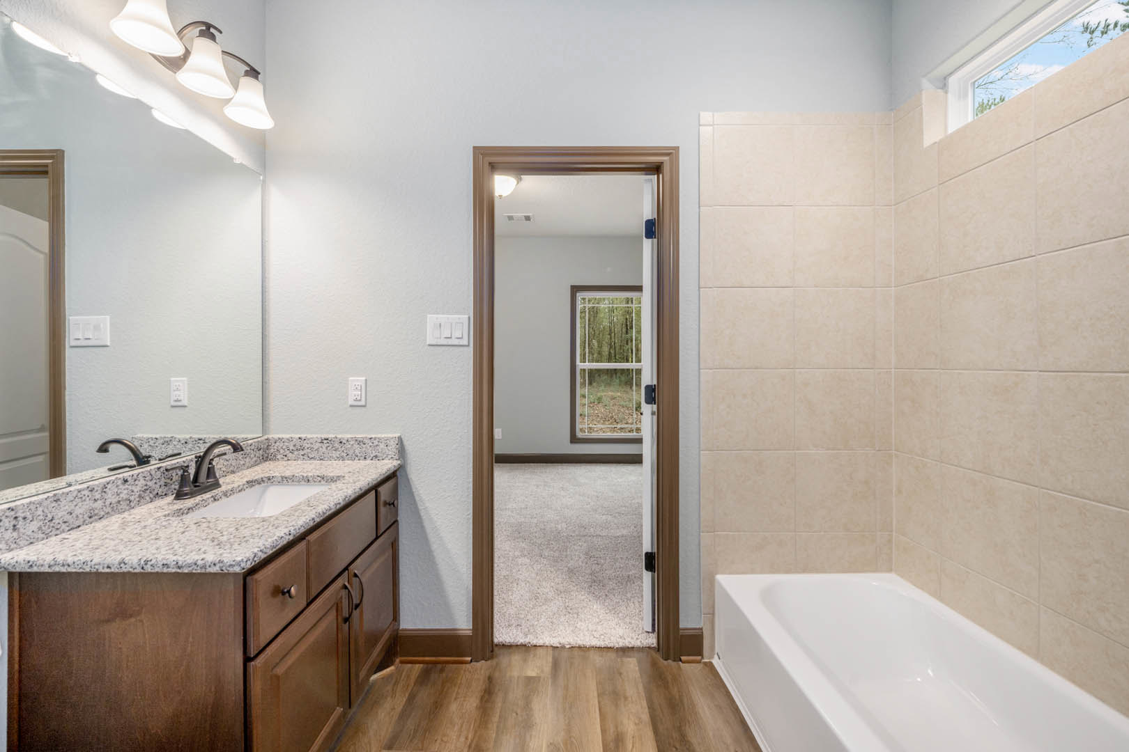 Bathroom featuring a freestanding white bathtub near a window overlooking a forest, modern sink with countertop and mirror, open door leading to adjacent room, and triple white