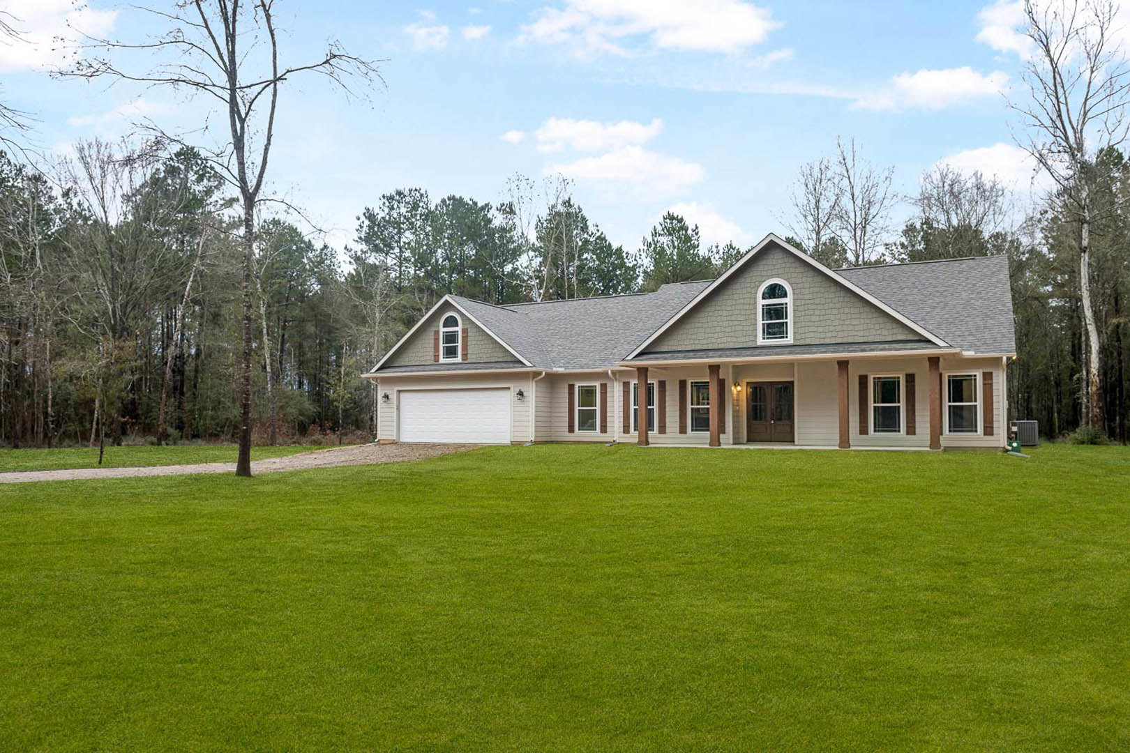 White two-story house with large windows, wide front door, expansive green lawn, white exterior walls with subtle stripes, mature trees in background, blue sky with scattered