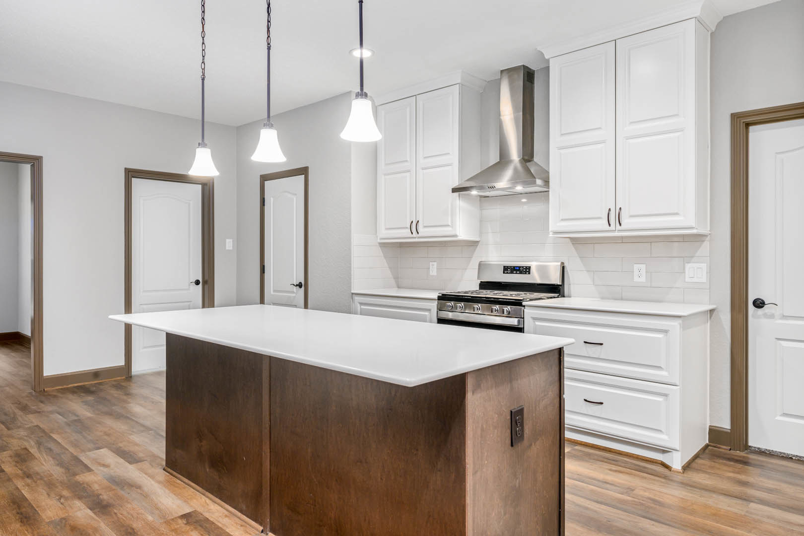 White kitchen with shaker cabinets, black handles, large central island with white countertop, stainless steel stove, vent hood, and undermount sink