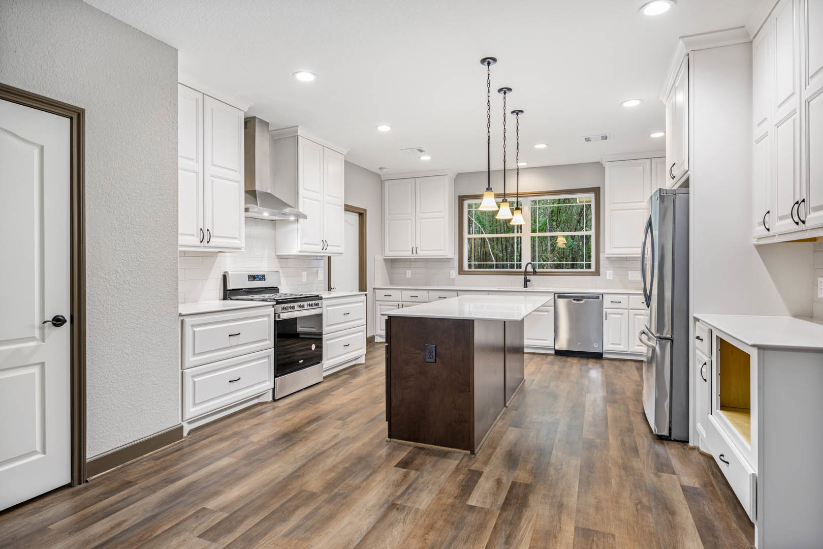 White shaker cabinets, stainless steel appliances, wood plank flooring, quartz countertops, undermount sink, pendant lights above kitchen island