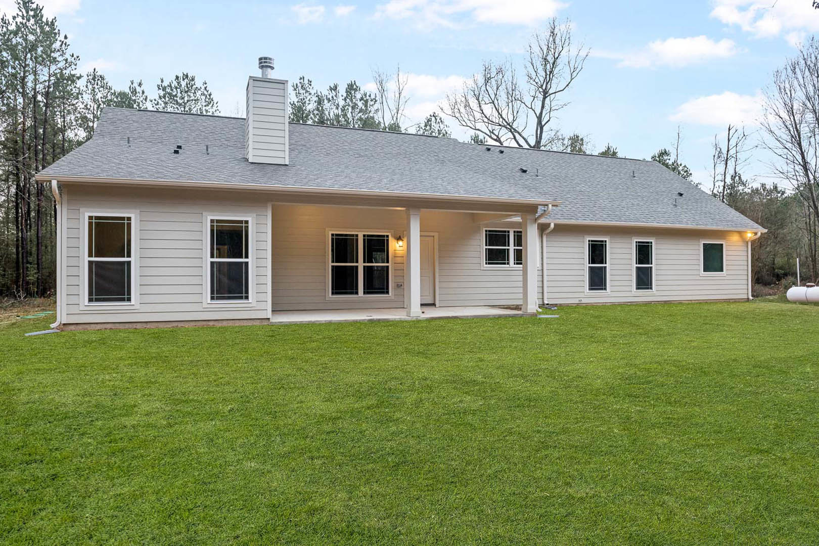 Gray two-story house with white trim, covered front porch, large windows, and manicured green lawn under partly cloudy sky