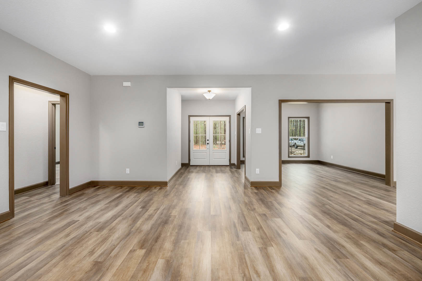 Hardwood floor room with white walls, double glass-paneled doors, and window showing parked white truck outside