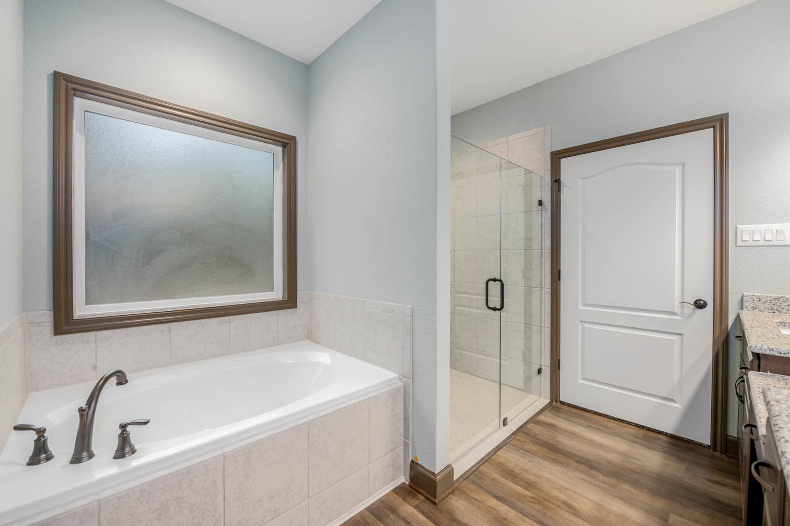 Bathroom with white tile walls, built-in bathtub and chrome faucet, glass shower enclosure, frosted window, white door with black handle, and four-switch light panel