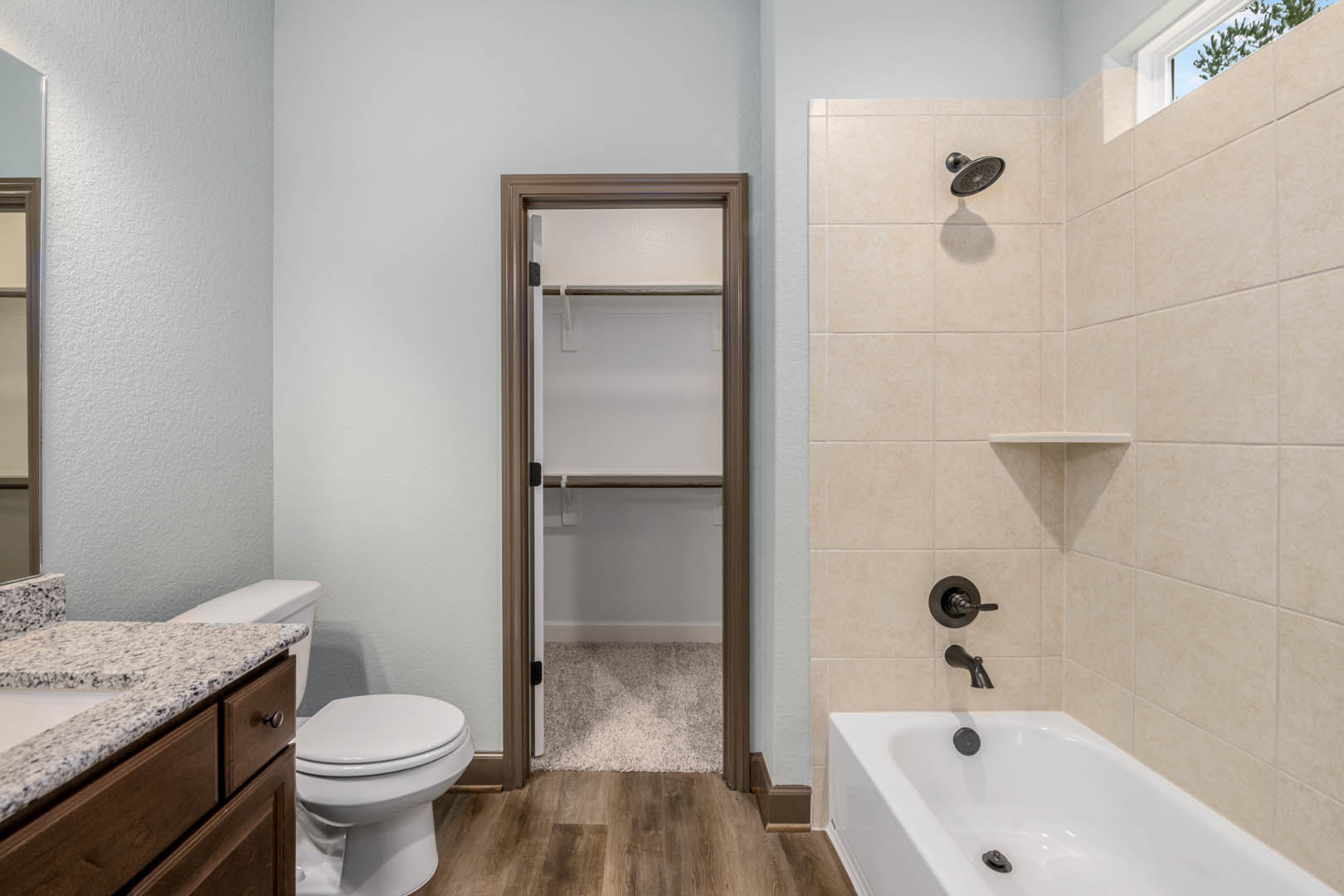 Bathroom with white toilet, marble countertop, built-in bathtub, and white closet door; tile flooring and neutral wall finishes.