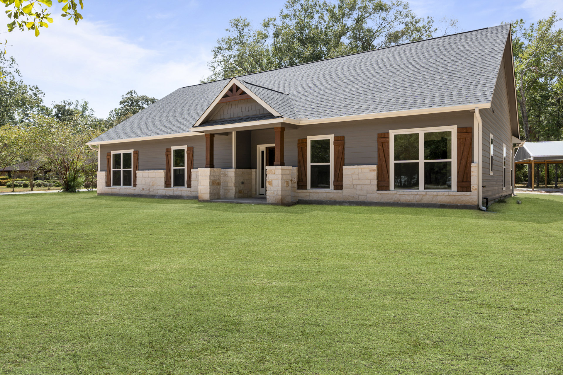 Two-story home with stone roof, white-framed windows, and columned porch, surrounded by green grass lawn and mature trees