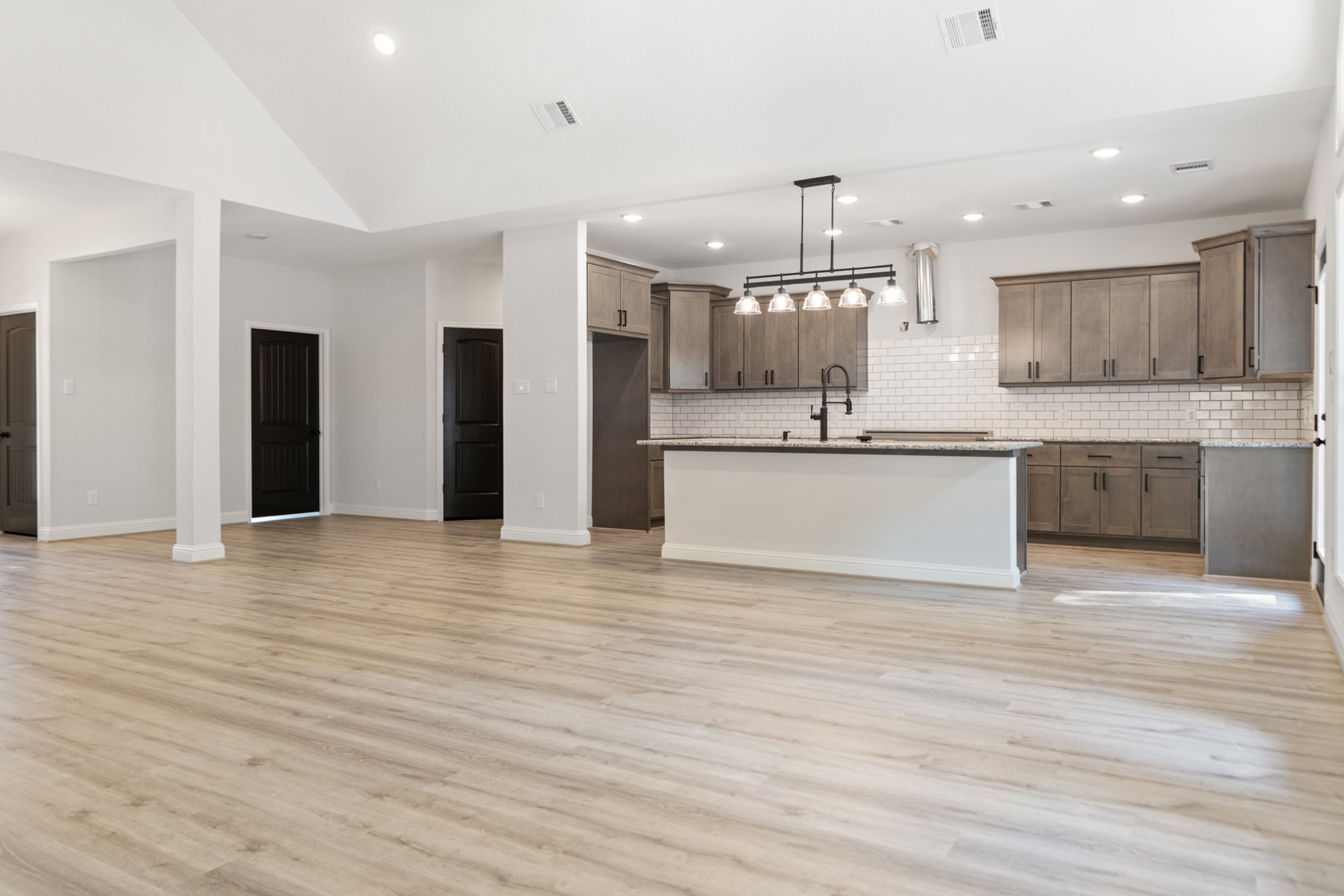 Open kitchen and living room with wood flooring, white walls, white cabinetry, marble countertop, black door with white frame, and grey accent wall with black trim.