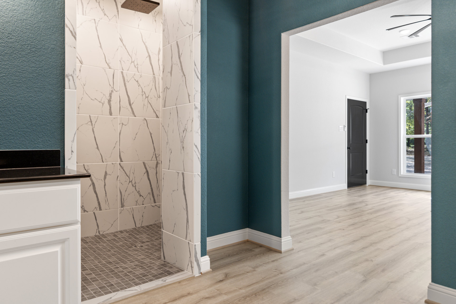 Bathroom featuring marble wall tiles, wood flooring, glass shower enclosure with linear drain, white-framed window, and modern cabinetry