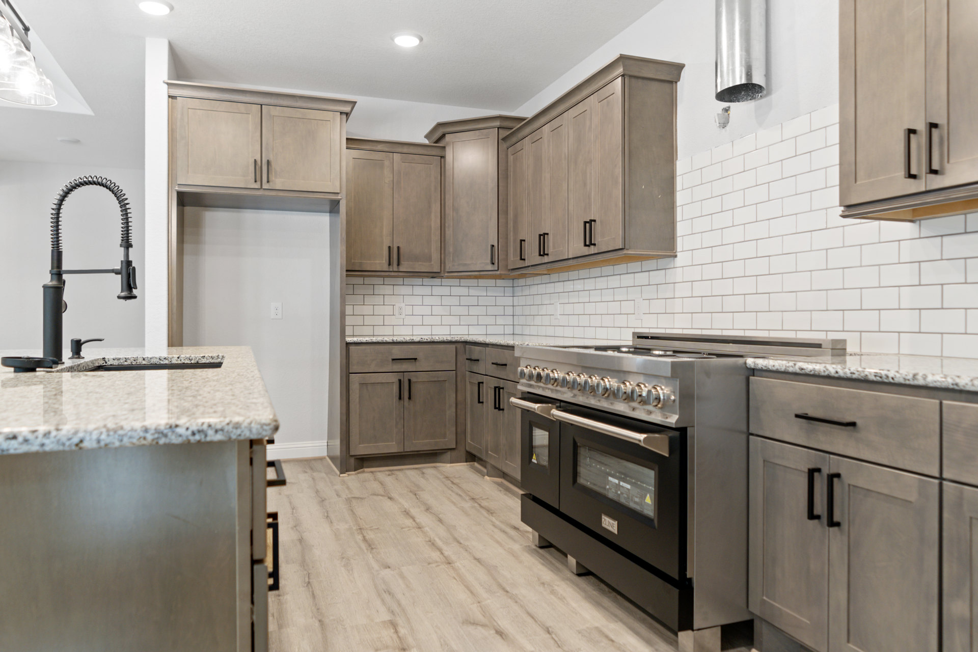 Modern kitchen with stainless steel stove and oven, white tile backsplash, black faucet with metal tubing, light wood cabinetry, and quartz countertop