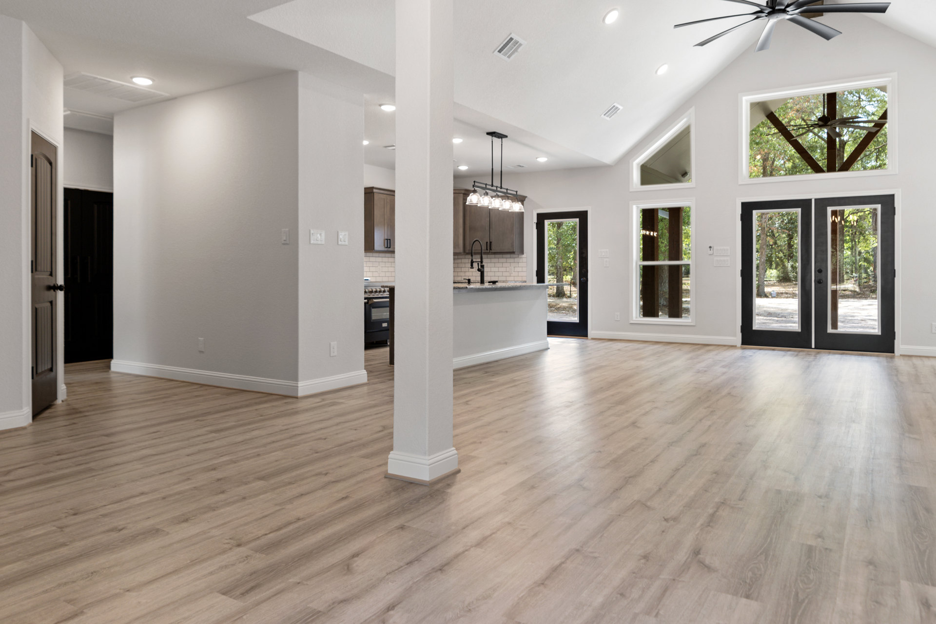 Wood flooring with white pillars, glass-paneled double doors, ceiling fan, and white vent on smooth white ceiling