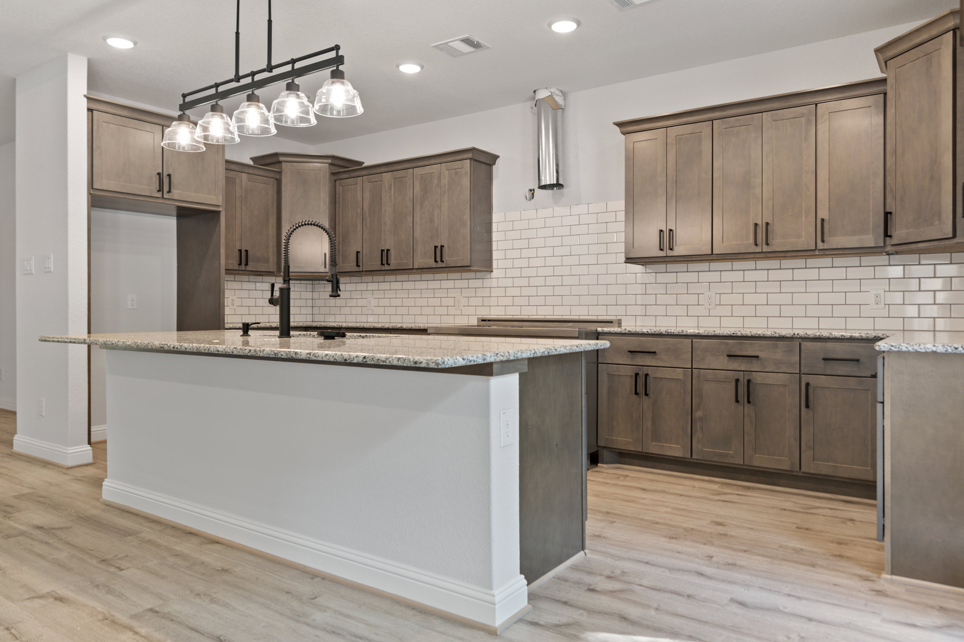 White kitchen with shaker cabinets, quartz island featuring undermount sink, stainless faucet, pendant lights with clear glass shades, hardwood flooring