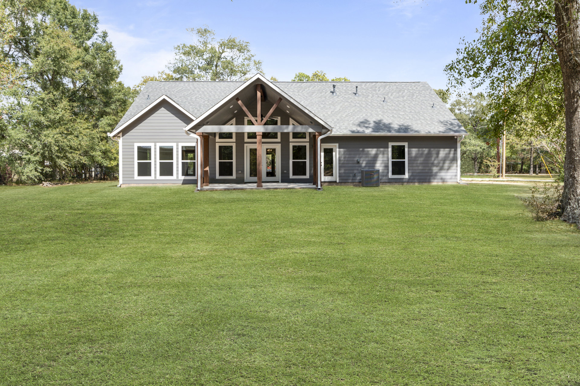 Two-story farmhouse with white siding, grey roof, covered front porch, large green lawn, white-framed windows, and mature trees under a partly cloudy sky