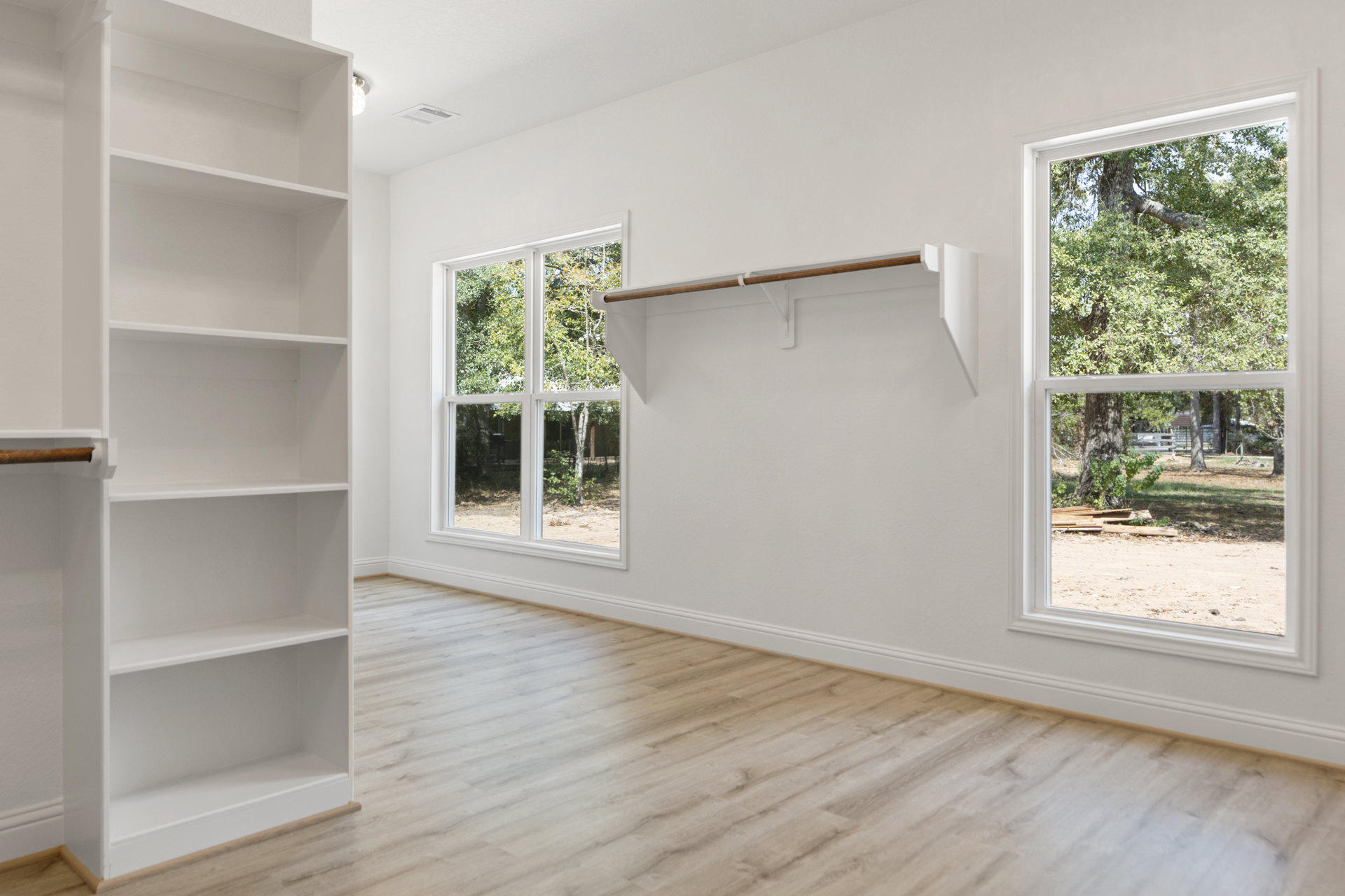 Wood floor room with built-in plywood shelves, large windows overlooking trees, and neutral walls.
