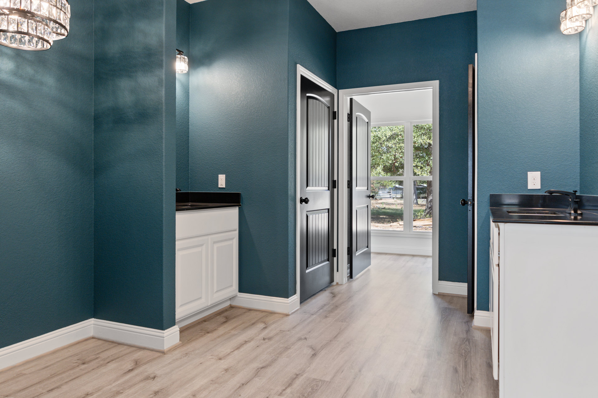 Hallway with deep blue walls, white cabinetry, light wood flooring, white refrigerator, open door leading to yard, modern chandelier overhead