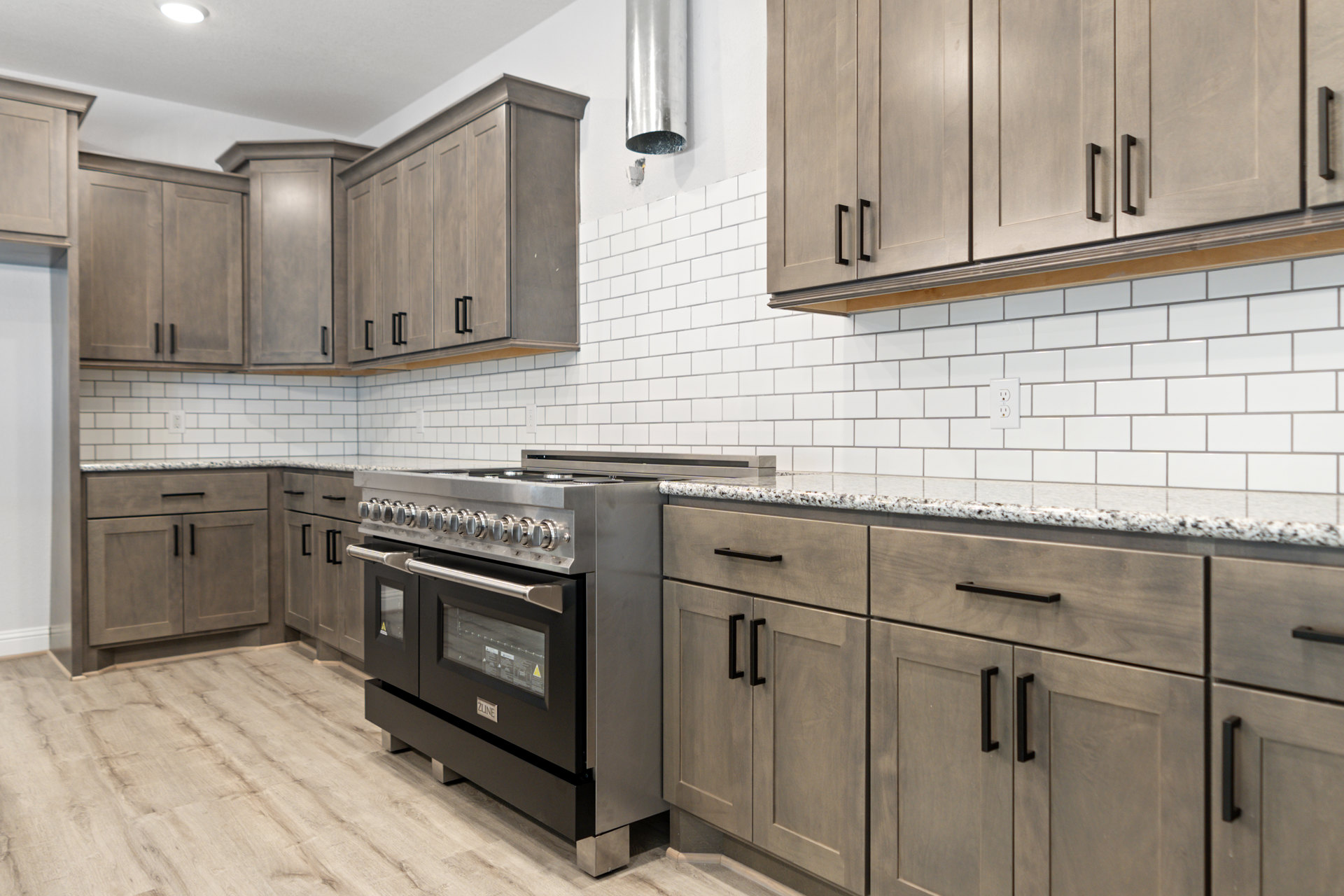 Kitchen with natural wood cabinets, stainless steel stove with glass door, tile backsplash, light countertops, and white walls.
