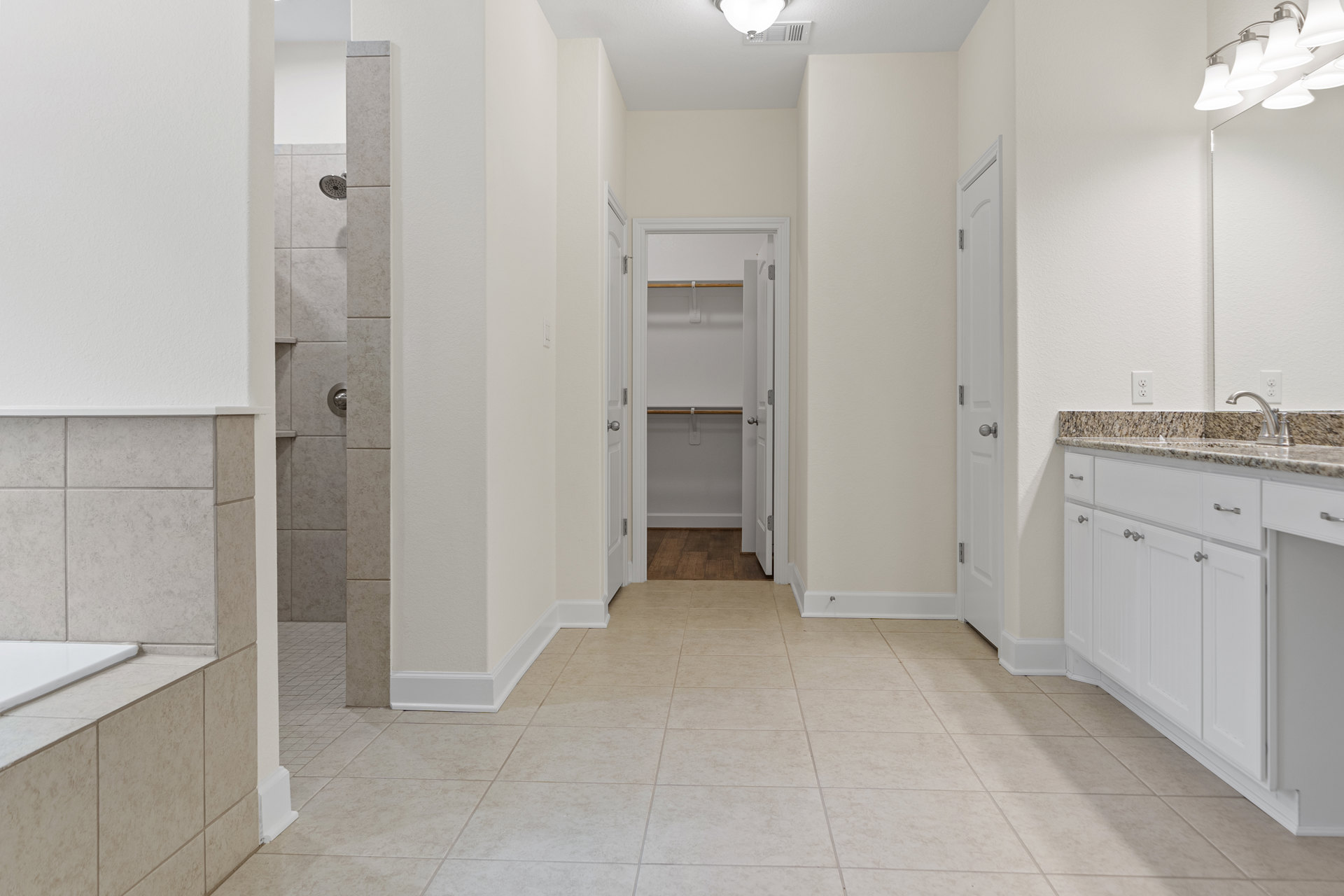 Hallway with white walls, white cabinetry, white tile floor, wood doors, silver door knobs, and silver cabinet handles