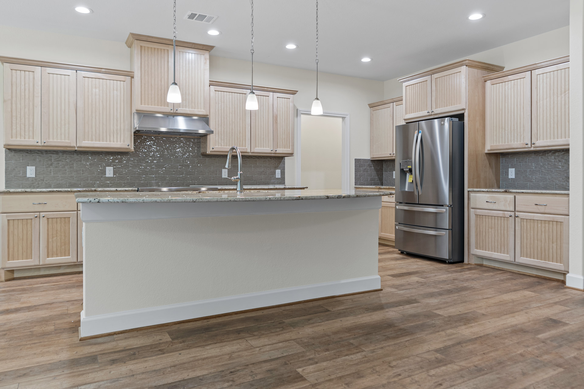 Kitchen with a marble-topped island, stainless steel appliances including a refrigerator with a yellow label, wood flooring, white walls, and modern cabinetry