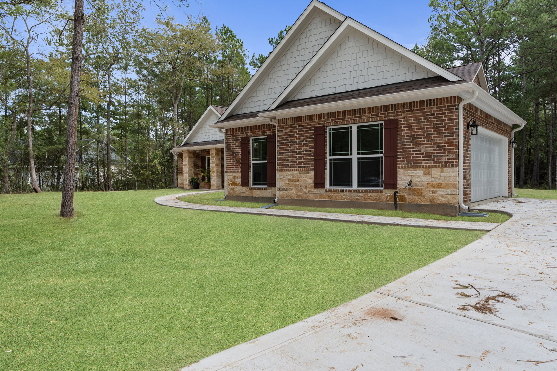 Red brick house with white-framed windows and shutters, wood and brick roof, front lawn with walkway, mature trees bordering property