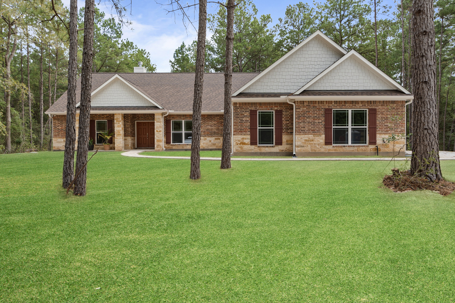 Red brick house with white-framed windows, glass-paneled door, green lawn, and mature trees under blue sky