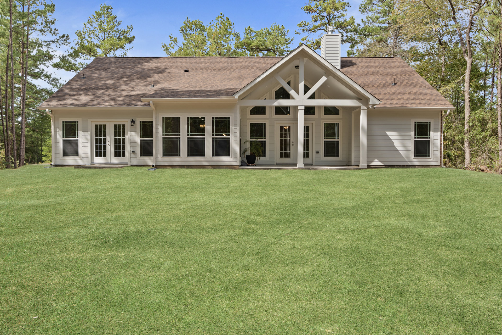 Two-story home with white framed windows, covered front porch, and manicured grass lawn bordered by a mature tree