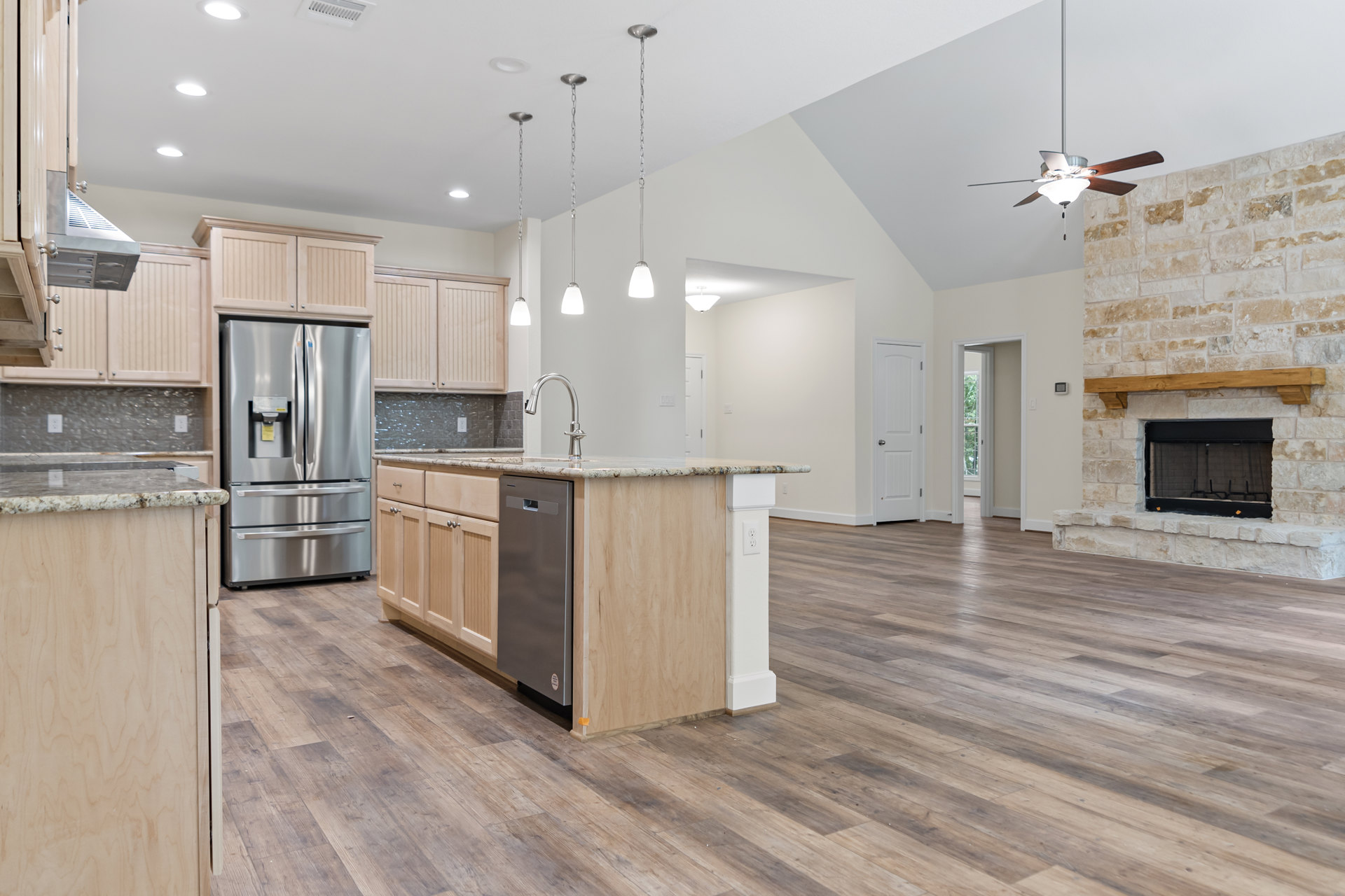 Open kitchen and living room with wood floors, silver refrigerator with paper label, black-framed fireplace, blackboard, chrome faucet, and paper towel dispenser