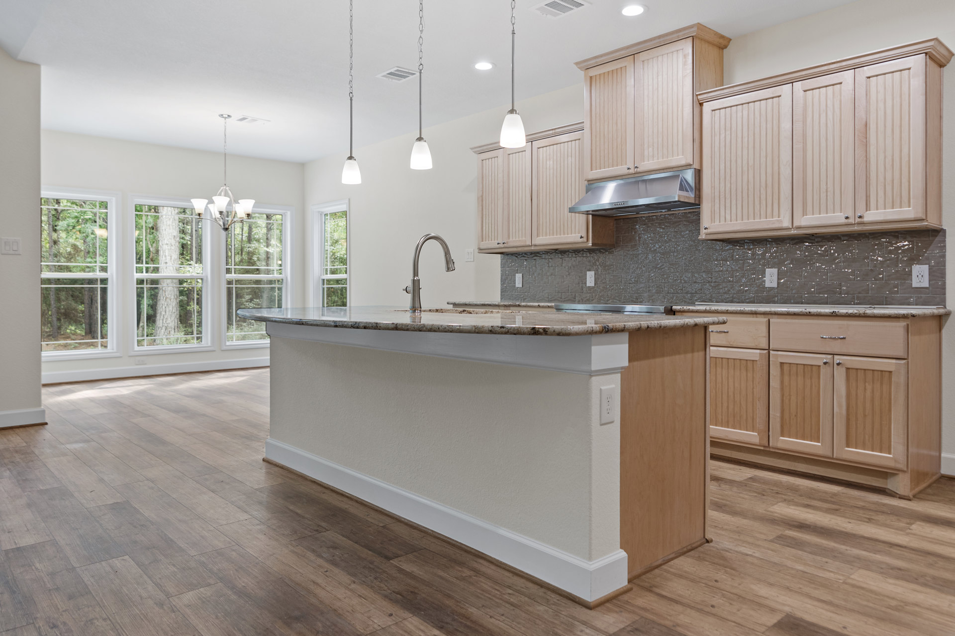 Kitchen with natural wood cabinets, expansive granite island, tile backsplash, stainless steel sink and faucet, pendant light fixtures, hardwood flooring, and large window