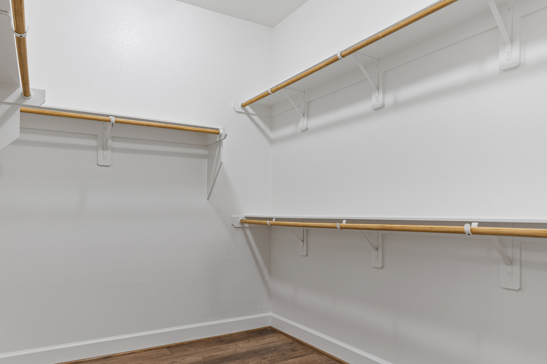 White closet with wooden shelves, wood floor, white baseboard, and metal hanging rod against plaster walls.