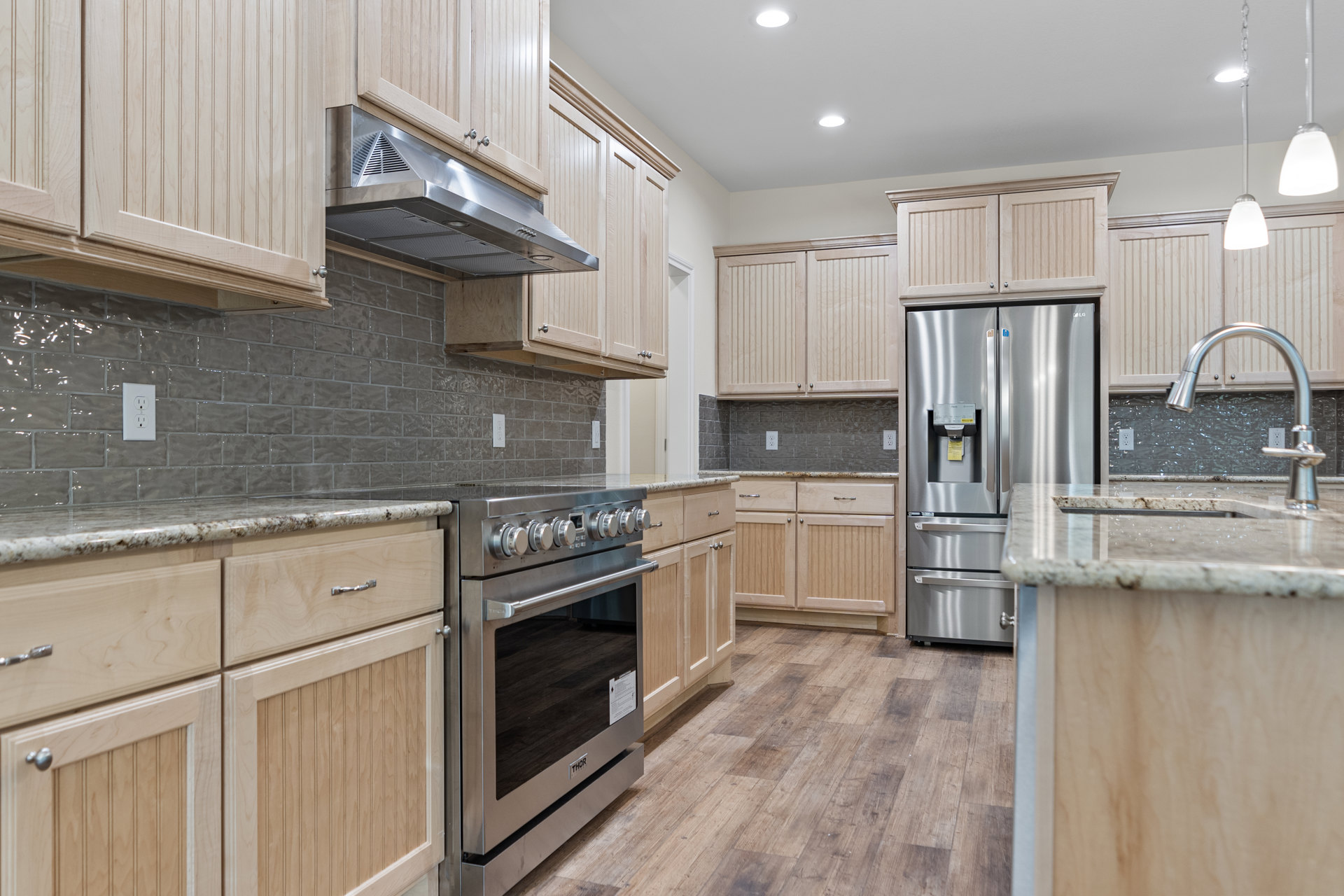 Kitchen with natural wood cabinets, stainless steel refrigerator and oven, range hood, white countertop, and visible electrical outlet on backsplash
